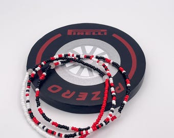 May include: Three beaded bracelets in red, black, and white colors. The bracelets are on top of a black tire with the word "PZERO" and the Pirelli logo.