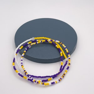 May include: A triple strand beaded necklace with purple, yellow, and white beads.