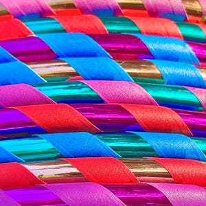 May include: Close-up of a colorful hoop with alternating stripes of red, pink, blue, and teal. The hoop is made of flexible plastic and has a shiny, metallic finish.