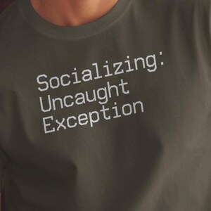 May include: A dark grey t-shirt with the text "Socializing: Uncaught Exception" printed in white.