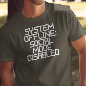May include: A dark green t-shirt with the text "SYSTEM: OFFLINE: SOCIAL MODE DISABLED" in white.