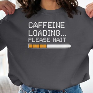 Może przedstawiać: Szara bluza z kapturem z napisem "CAFFEINE LOADING... PLEASE WAIT" w kolorze białym i paskiem postępu z pomarańczowymi paskami.