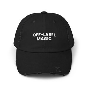 May include: Black baseball cap with distressed details. The cap features the text "OFF-LABEL MAGIC" in white block letters across the front. A stylish and casual accessory.