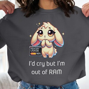 May include: A grey sweatshirt featuring a cartoon bunny rabbit wearing a pink headband. The bunny is holding its paws together and has a sad expression. The text "MEMORY USAGE 98%" is displayed in a blue box with a red progress bar. The text "I'd cry but I'm out of RAM" is displayed below the bunny.