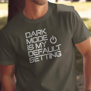 May include: A dark green t-shirt with white text that reads "DARK MODE IS MY DEFAULT SETTING" and a power button symbol.