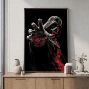 Könnte beinhalten: Ein gerahmter, vertikaler Wandkunstdruck mit einer dunklen, stilisierten Illustration von Darth Vader, der seine behandschuhte Hand ausstreckt. Die Figur ist in Schwarz- und Grautönen mit markanten roten Akzenten vor schwarzem Hintergrund.