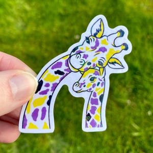 May include: A sticker featuring two giraffes, one adult and one juvenile, with a white outline. The giraffes have a pattern of purple, yellow, and black spots. The background is blurred green grass.