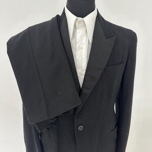 Könnte beinhalten: Ein schwarzer Anzugjackett mit einem Satinrevers und einem einzigen Knopfverschluss. Die Jacke befindet sich auf einem Mannequin und wird mit einem weißen Hemd kombiniert.