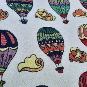 May include: A fabric with a repeating pattern of colorful hot air balloons and yellow cloud shapes on a light background. The balloons feature intricate designs in red, green, blue, and purple.