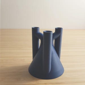 以下が含まれることがあります： 円錐形のベースと3つの円筒形のアームを備えた、濃い青色のモダンなキャンドルホルダー。アームは上方に伸び、ミニマリストなデザインを作り出しています。キャンドルホルダーはマットな素材で作られています。