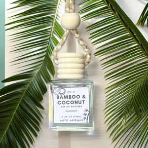 May include: A clear glass car air freshener with a wooden top and a string for hanging. The label reads "NO. 2 BAMBOO & COCONUT CAR OIL DIFFUSER 0.35 OZ. (10ML) AUTO AROMAS".