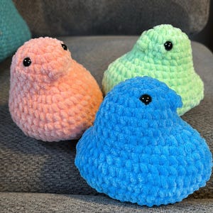 May include: Three crocheted plush toys shaped like Peeps, a popular marshmallow candy. The toys are in pink, green, and blue.