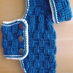May include: A blue knitted dog sweater with white trim and three buttons. The sweater has a matching blue knitted collar.