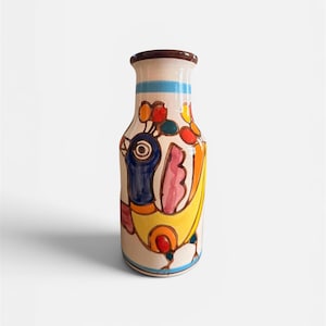 May include: A ceramic vase with a cream-colored base featuring a hand-painted, stylized bird design in vibrant shades of blue, yellow, pink, and orange. The vase has a narrow neck with a brown rim and a light blue horizontal band near the top.