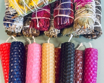 May include: An assortment of dried sage bundles adorned with colorful flowers and tied with twine, alongside a collection of honeycomb-patterned pillar candles in various colors, including red, blue, pink, and black. The candles have a textured surface.
