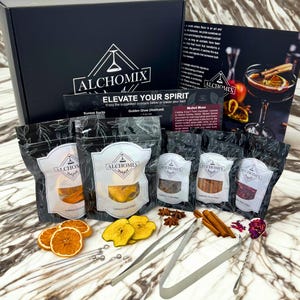 May include: A black gift box with the Alchomix logo and the text "ELEVATE YOUR SPIRIT". The box contains cocktail ingredients, including dried fruit, spices, and bar tools. The image also shows a cocktail recipe card.