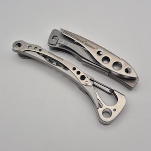 Puede incluir: Dos multiherramientas plateadas con la marca "LEATHERMAN". Una está abierta, mostrando una cuchilla, la otra está cerrada. Ambas tienen un diseño esquelético con agujeros y un mosquetón. Herramientas de metal.