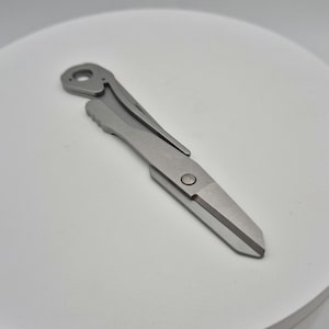 Könnte beinhalten: Ein silbernes Multitool mit einer kleinen Klinge und einem Flaschenöffner. Das Werkzeug ist kompakt und einfach zu transportieren.