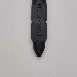 May include: A black Phillips head screwdriver bit with the text "NO.2 NO.1" printed on the side. The bit has a pointed tip and is designed for use with a screwdriver. The tool is shown against a white background.