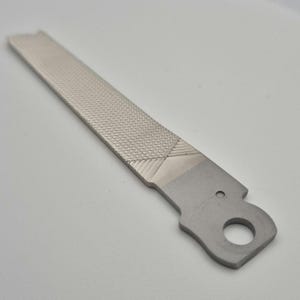 Pode incluir: Uma lima de metal prateada com uma superfície texturizada e um furo no cabo.
