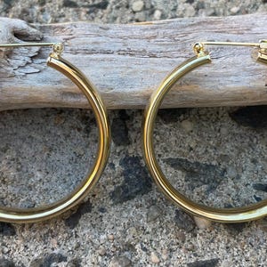 May include: A pair of large, gold-toned hoop earrings. The hoops are thick and have a smooth, polished finish.