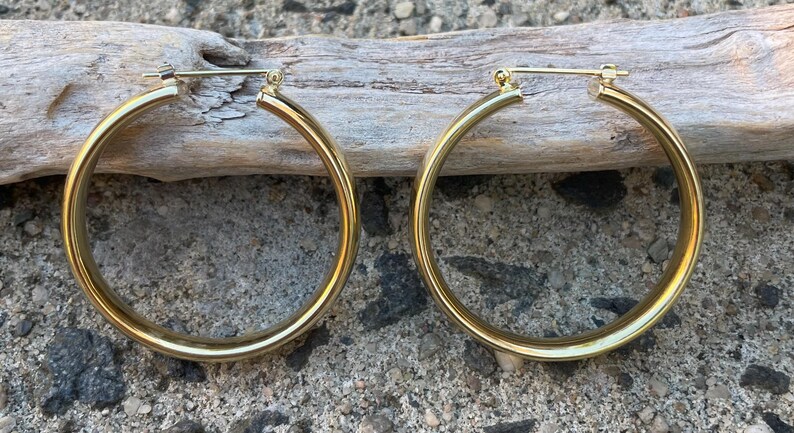 May include: A pair of large, gold-toned hoop earrings. The hoops are thick and have a smooth, polished finish.