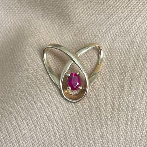 Puede incluir: Un colgante de oro con una piedra preciosa de rubí rojo engastada en un diseño delicado e entrelazado.