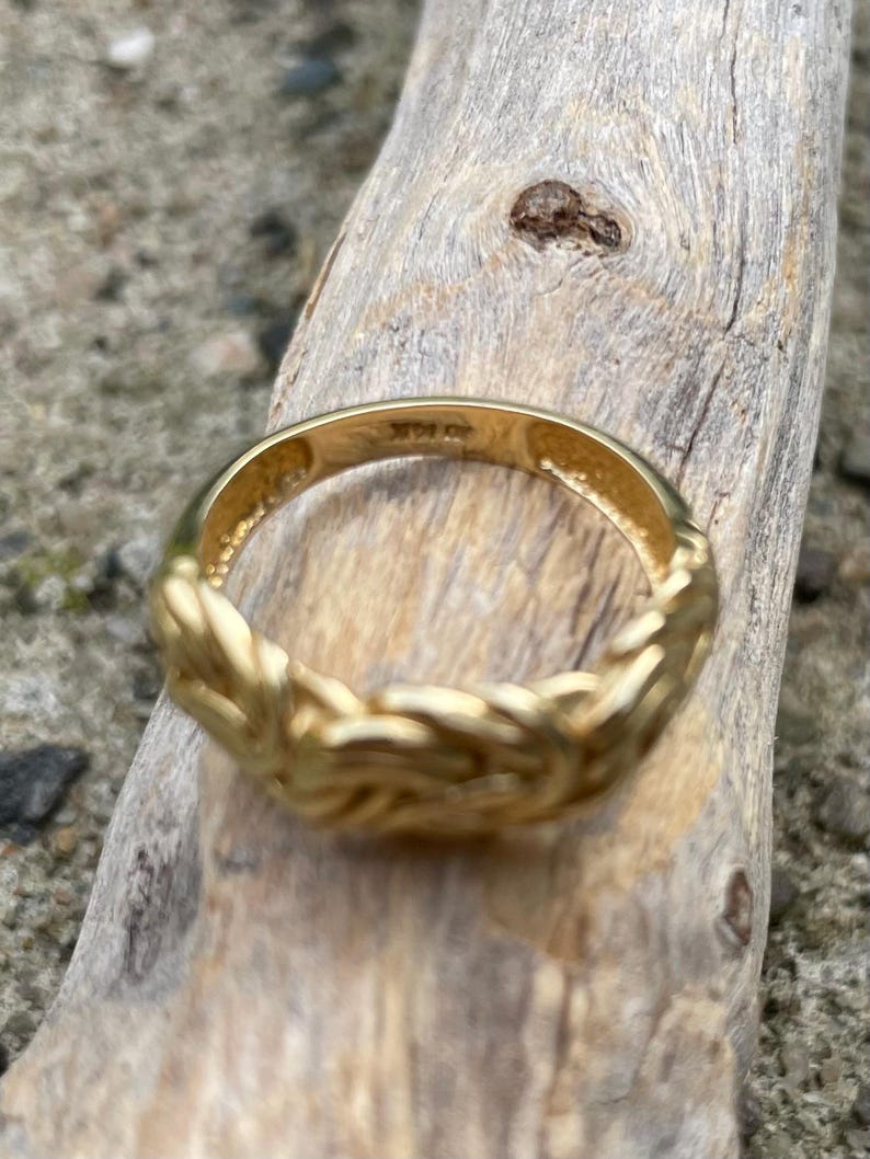 Puede incluir: Un anillo de color dorado con un dise&ntilde;o trenzado. El anillo est&aacute; sobre una superficie de madera.