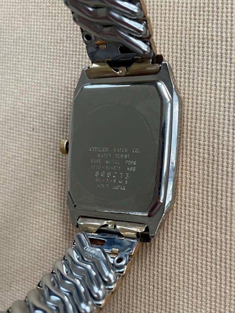 Peut inclure: Une montre Citizen argent&eacute;e et dor&eacute;e avec un cadran carr&eacute; et un bracelet en m&eacute;tal. Le dos de la montre porte l'inscription "CITIZEN WATCH CO. WATER RESIST BASE METAL FOFE 1000-885871 HSE 809213 28-0-845 MINT JAPAN".