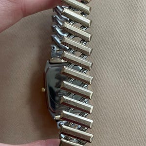 Peut inclure: Une montre argent&eacute;e et dor&eacute;e avec un cadran carr&eacute; et un bracelet en m&eacute;tal bicolore. Le bracelet est compos&eacute; de maillons rectangulaires.