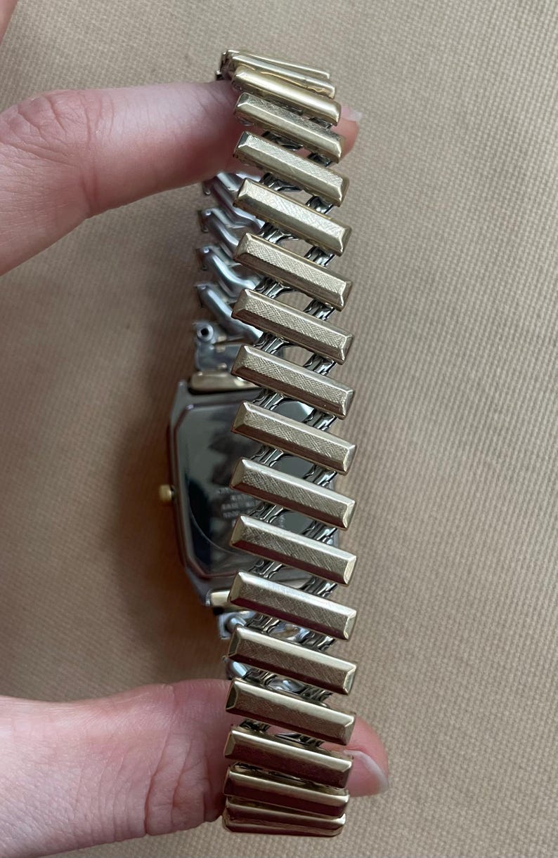 Peut inclure: Une montre argent&eacute;e et dor&eacute;e avec un cadran carr&eacute; et un bracelet en m&eacute;tal bicolore. Le bracelet est compos&eacute; de maillons rectangulaires.