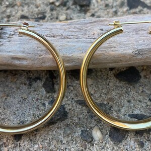 May include: A pair of gold hoop earrings. The earrings are thick and have a smooth, polished finish.