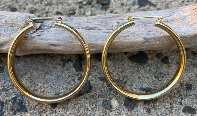 May include: A pair of gold hoop earrings. The earrings are thick and have a smooth, polished finish.