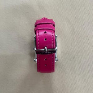 Puede incluir: Una correa de reloj de cuero rosa con una hebilla plateada. La hebilla tiene la palabra "WISTER" grabada.