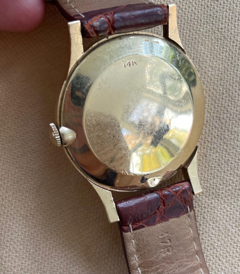 May include: Close-up of a vintage gold wristwatch with a brown leather band. The watch case is gold-toned with the marking "14K" visible. The band is a dark brown color.