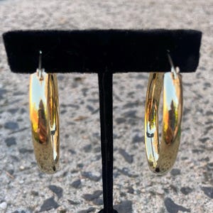 May include: A pair of gold hoop earrings. The earrings are large and have a smooth, polished finish.