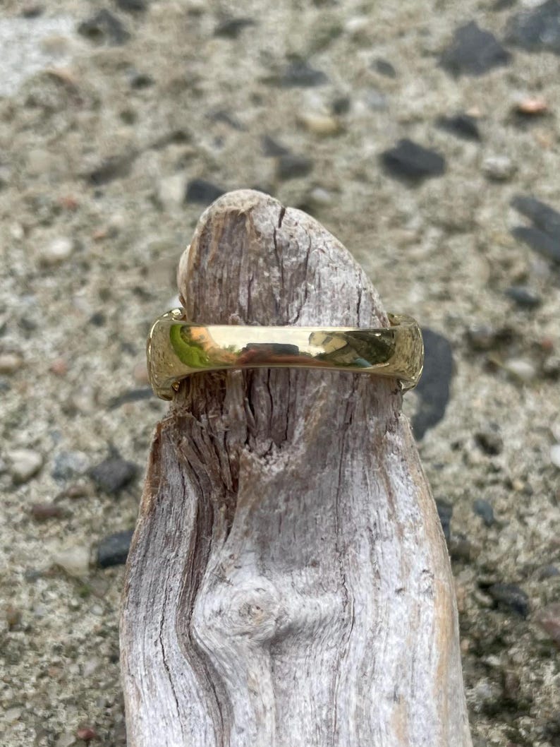 Puede incluir: Un anillo de color dorado con una superficie lisa y redondeada. El anillo est&aacute; sentado en un trozo de madera a la deriva.