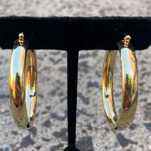 May include: A pair of gold hoop earrings. The hoops are thick and have a shiny finish.