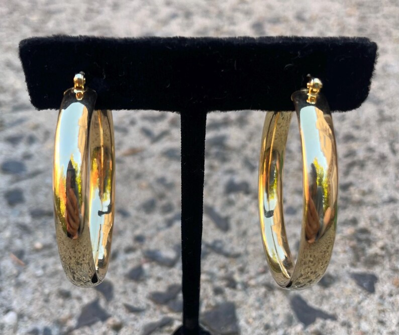 May include: A pair of gold hoop earrings. The hoops are thick and have a shiny finish.