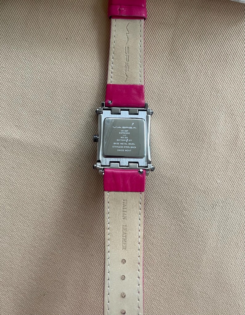 Puede incluir: Un reloj plateado con una esfera cuadrada y una correa de cuero rosa. La esfera del reloj tiene el texto "MA SPIGA" y "ESPRESSO" en ella. La correa tiene el texto "ITALIAN LEATHER" en ella.