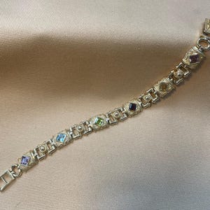 May include: A gold bracelet with a geometric design and colorful gemstones. The bracelet has a clasp closure.