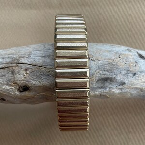 Peut inclure: Un bracelet de montre en m&eacute;tal dor&eacute; avec un design textur&eacute; et stri&eacute;. Le bracelet est flexible et r&eacute;glable.