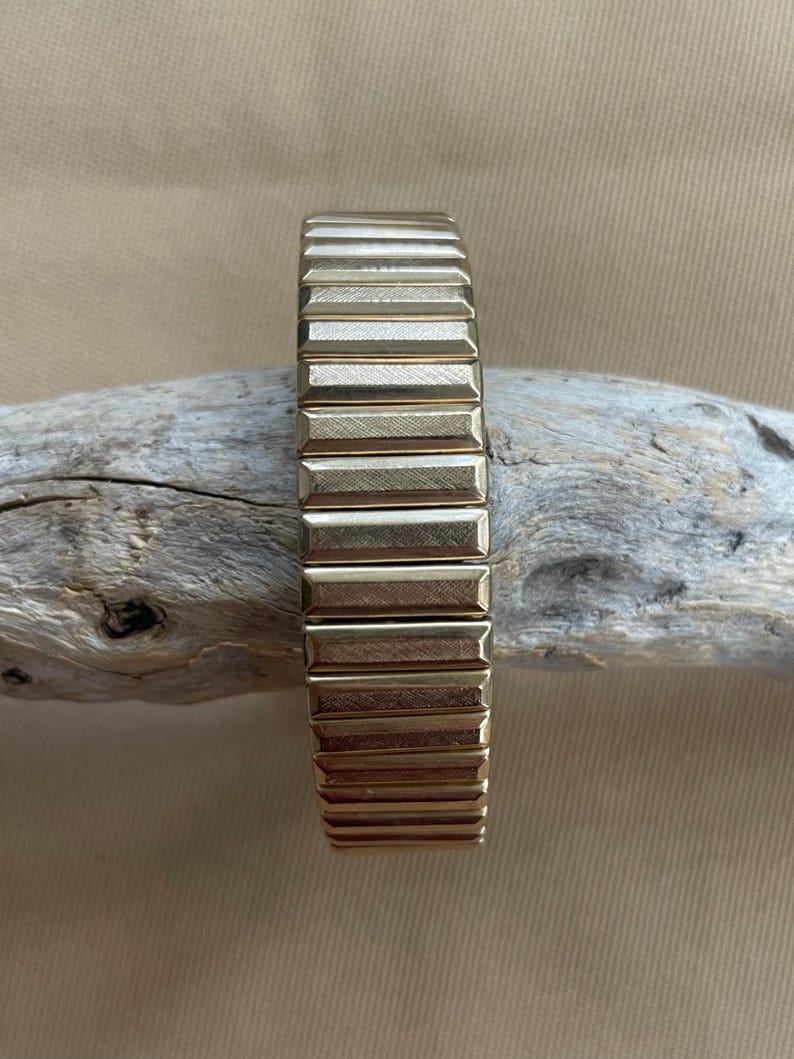 Peut inclure: Un bracelet de montre en m&eacute;tal dor&eacute; avec un design textur&eacute; et stri&eacute;. Le bracelet est flexible et r&eacute;glable.