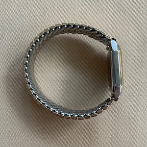 Peut inclure: Une montre argent&eacute;e avec un cadran carr&eacute; et un bracelet en m&eacute;tal argent&eacute;. Le bracelet est compos&eacute; de petites pi&egrave;ces reli&eacute;es qui cr&eacute;ent un ajustement flexible et confortable.