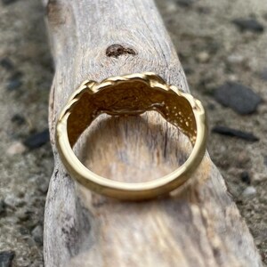Puede incluir: Un anillo de color dorado con un dise&ntilde;o texturizado e irregular. El anillo est&aacute; sobre una pieza de madera desgastada.