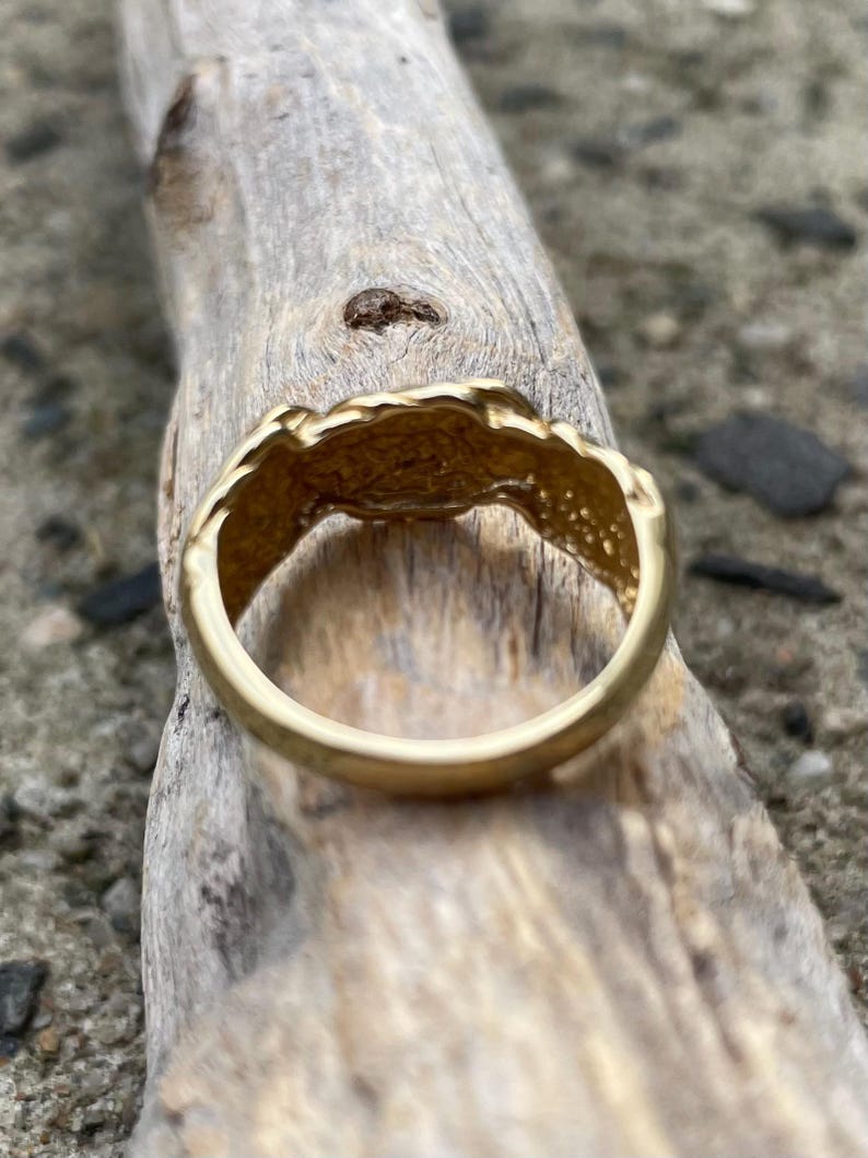 Puede incluir: Un anillo de color dorado con un dise&ntilde;o texturizado e irregular. El anillo est&aacute; sobre una pieza de madera desgastada.