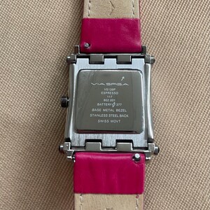Puede incluir: Un reloj plateado con una correa de cuero rosa. La esfera del reloj es rectangular y tiene un bisel plateado. La esfera del reloj es negra y tiene el texto "VIA SPIGA VS139P ESPRESSO 117 802.001 BATTERY 377 BASE METAL BEZEL STAINLESS STEEL BACK SWISS MOVT ITALIAN" impreso en ella.