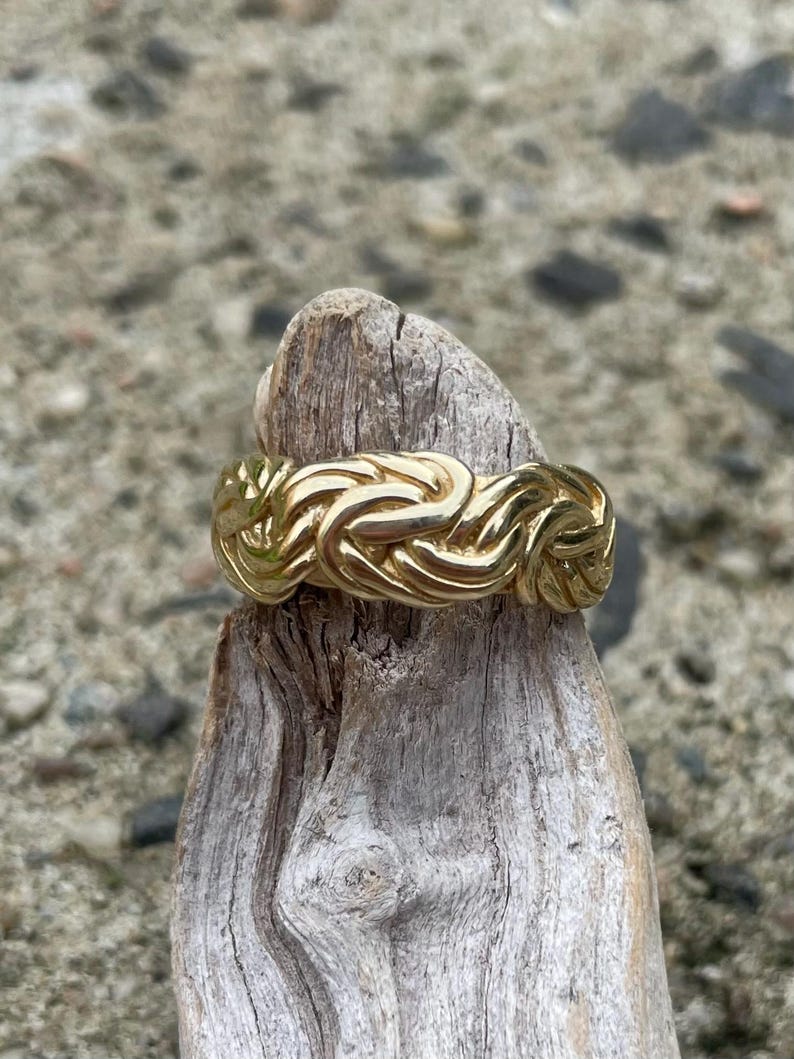 Puede incluir: Un anillo de color dorado con un dise&ntilde;o trenzado. El anillo est&aacute; sentado en un trozo de madera a la deriva.
