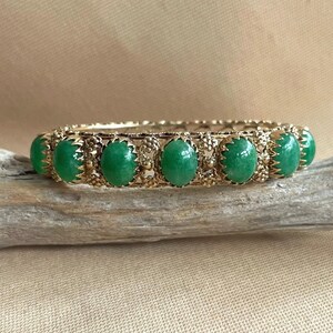 May include: A gold bangle bracelet with five green oval cabochon stones set in a filigree design.