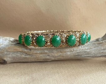 May include: A gold bangle bracelet with five green oval cabochon stones set in a filigree design.